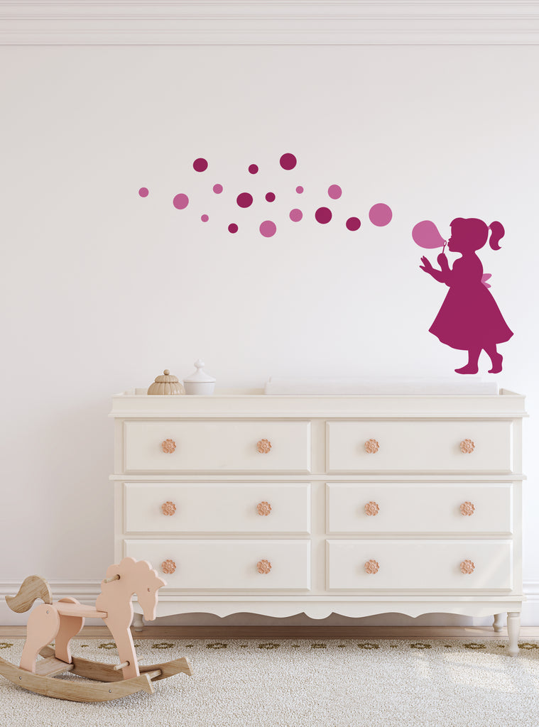 Bubble Girl Decal featuring a whimsical silhouette of a child blowing bubbles, displayed in pink against a white wall above a classic white dresser. Two streams of floating bubbles create a playful trail across the wall, perfect for nursery or children's room decor. Wall Decals, Baby Nursery and Kids Wall Decals, All Products, Top Sellers.