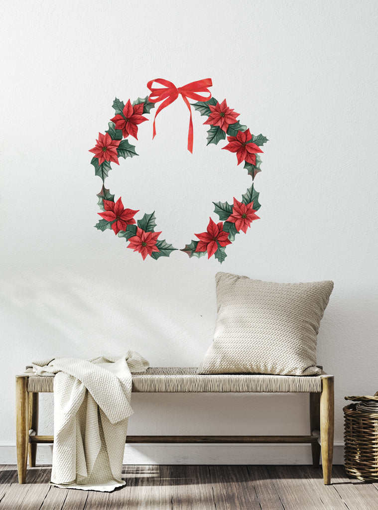 Festive Wreath Wall Sticker featuring red poinsettias and green holly leaves arranged in a circular shape, topped with a vibrant red bow, displayed on a white wall above a wooden bench with a cozy pillow and blanket, perfect for holiday home decor, Top Sellers,Wall Stickers,All Products