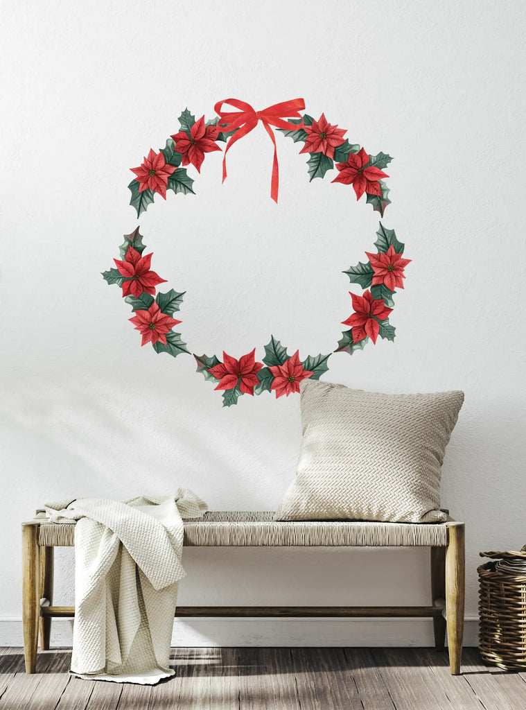 Festive Wreath Wall Sticker with red poinsettias, green leaves, and a red bow displayed on a white wall above a wooden bench with a neutral cushion and throw blanket, creating a cozy holiday atmosphere. Wreath Wall Sticker, Top Sellers, Wall Stickers, All Products