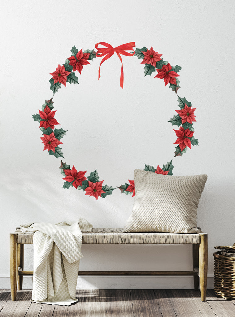 Festive Wreath Wall Sticker featuring vibrant red poinsettias and green holly leaves arranged in a circular shape with a red bow on top, displayed on a white wall above a rustic bench with cozy pillows and blanket, perfect for holiday home decor. Wreath Wall Sticker, Top Sellers, Wall Stickers, All Products