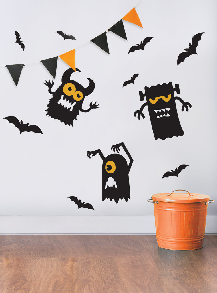 Halloween Monster Decals featuring playful black cartoon monsters with orange eyes and black flying bats against a white wall, accompanied by black and orange triangle bunting. Modern Halloween wall decorations perfect for spooky home decor. Featured in Wall Decals, All Products.