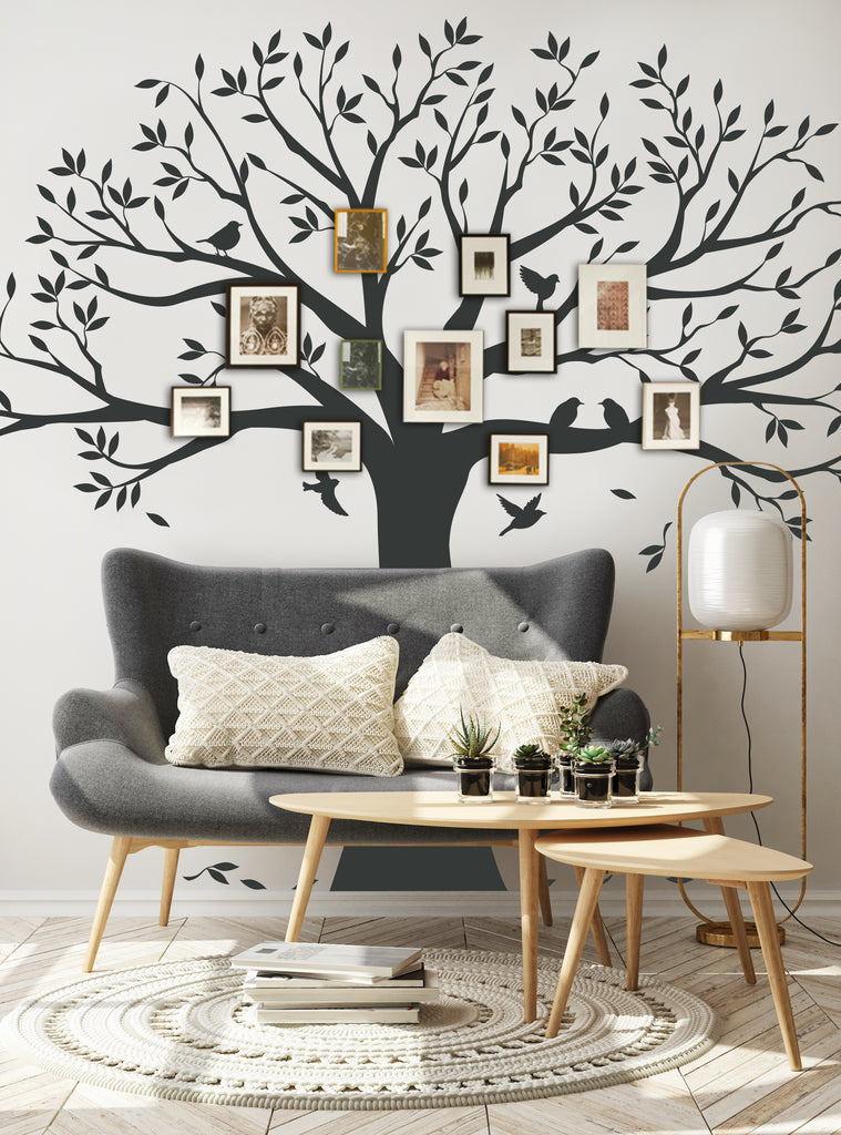 Large black tree wall decal with branches spreading across white wall, adorned with family photos in various frames. Gray couch and wooden tables in foreground create cozy living room setting. Perfect for displaying cherished memories. Featured Collection,Top Sellers,Wall Decals,Family Tree Decals,Tree Decals,All Products