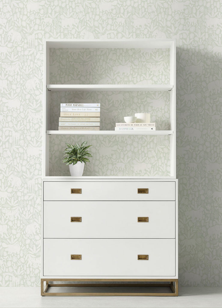 Stylish white bookshelf with drawers featuring gold accents, displaying books, a plant, and a cup on its shelves. Perfect backdrop for Jungle Animal Sage Fabric Peel and Stick Wallpaper OFF PRINT 24 x 108 Inches, Clearance Wallpaper Sticker - OFF PRINTS, Dorm Room Ideas and Trends