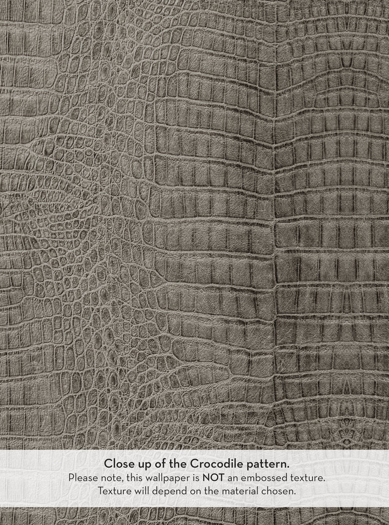 A close-up view of a grey crocodile-patterned wallpaper. The image showcases the intricate details of the pattern, highlighting the scales and texture. A note at the bottom explains that the wallpaper is not embossed and that the texture may vary depending on the chosen material. The overall design conveys a sophisticated and modern aesthetic.