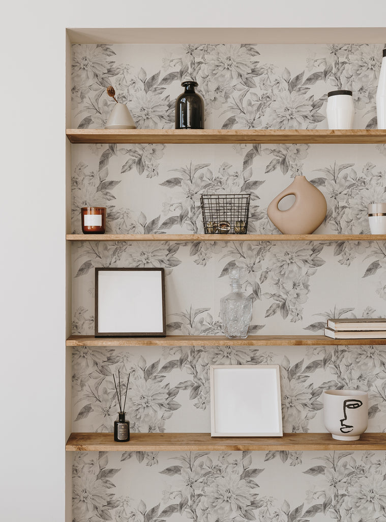 This image features a black and white floral wallpaper that creates a soft, elegant backdrop for the various decor items displayed on the shelves. The wallpaper pattern creates a beautiful, calming atmosphere and invites the viewer to imagine the soft, quiet beauty of blooming flowers in the space. The shelves hold a variety of decorative items, including vases, candles, and framed artwork, adding visual interest and personality to the space. Thi