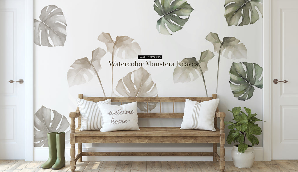 A rustic wooden bench with white pillows sits against a wall with watercolor Monstera leaf stickers. A pair of green rain boots is placed on the floor beside the bench, and a potted plant is nearby.